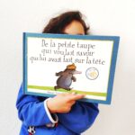 Couverture de l'album De la petite taupe qui voulait savoir qui lui avait fait sur la tête, illustrée par Wolf Erlbruch. On y voit une petite taupe noire, debout sur un monticule de terre, arborant une expression déterminée. Une crotte marron repose sur sa tête. Le fond est blanc, et le titre du livre est inscrit en haut de l'image.