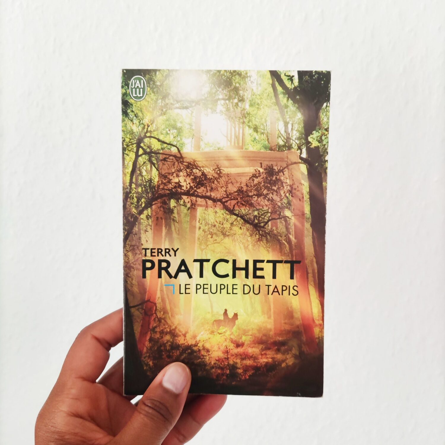 Couverture du roman Le Peuple du Tapis de Terry Pratchett, tenu sur fond blanc – livre de fantasy humoristique racontant la vie d’un peuple miniature vivant dans un tapis.